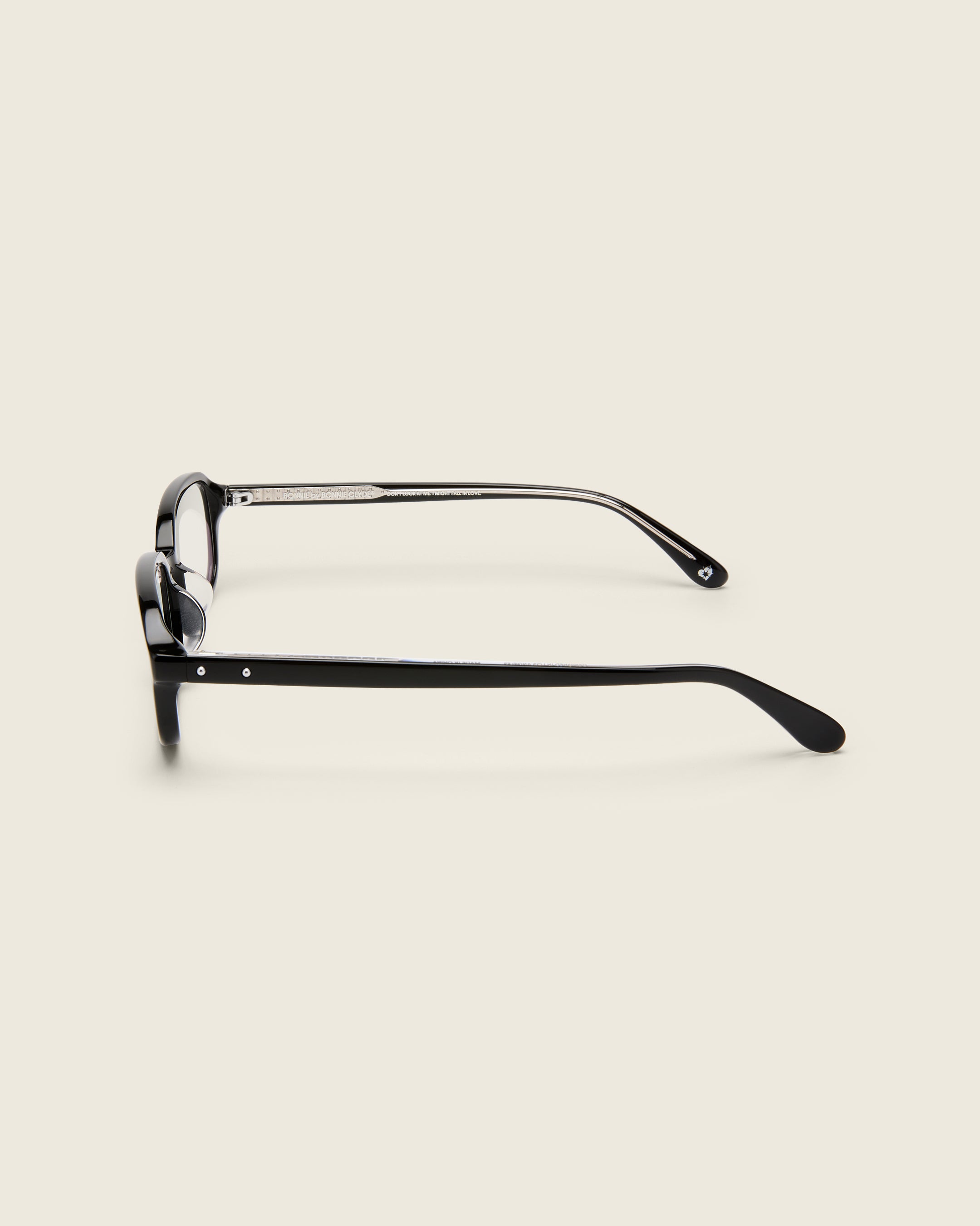 Rectangular black acetate frames with softened corners and a low-profile bridge on a beige background. Side view.