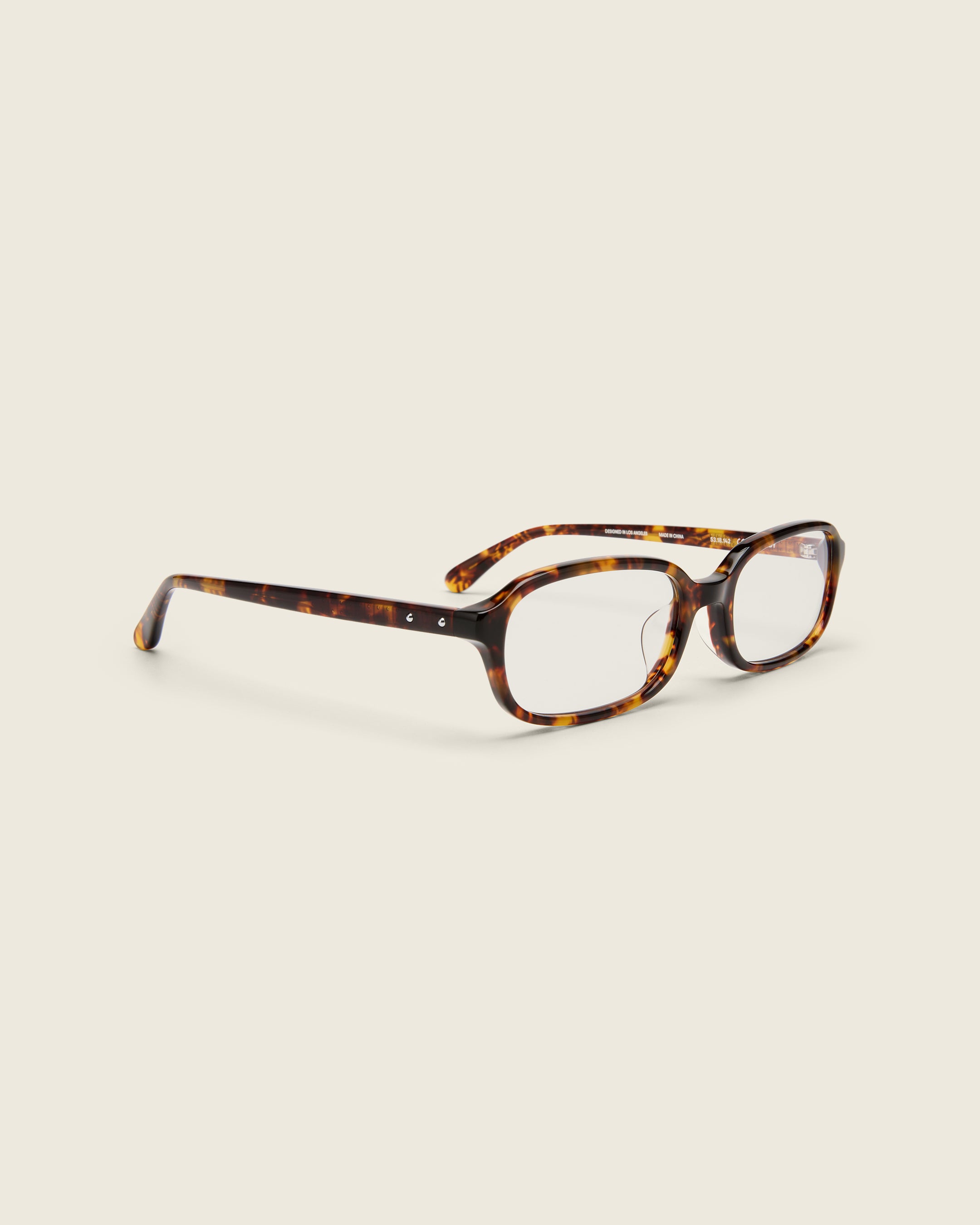 Rectangular tortoise acetate frames with softened corners and a low-profile bridge on a beige background. Quarter view.