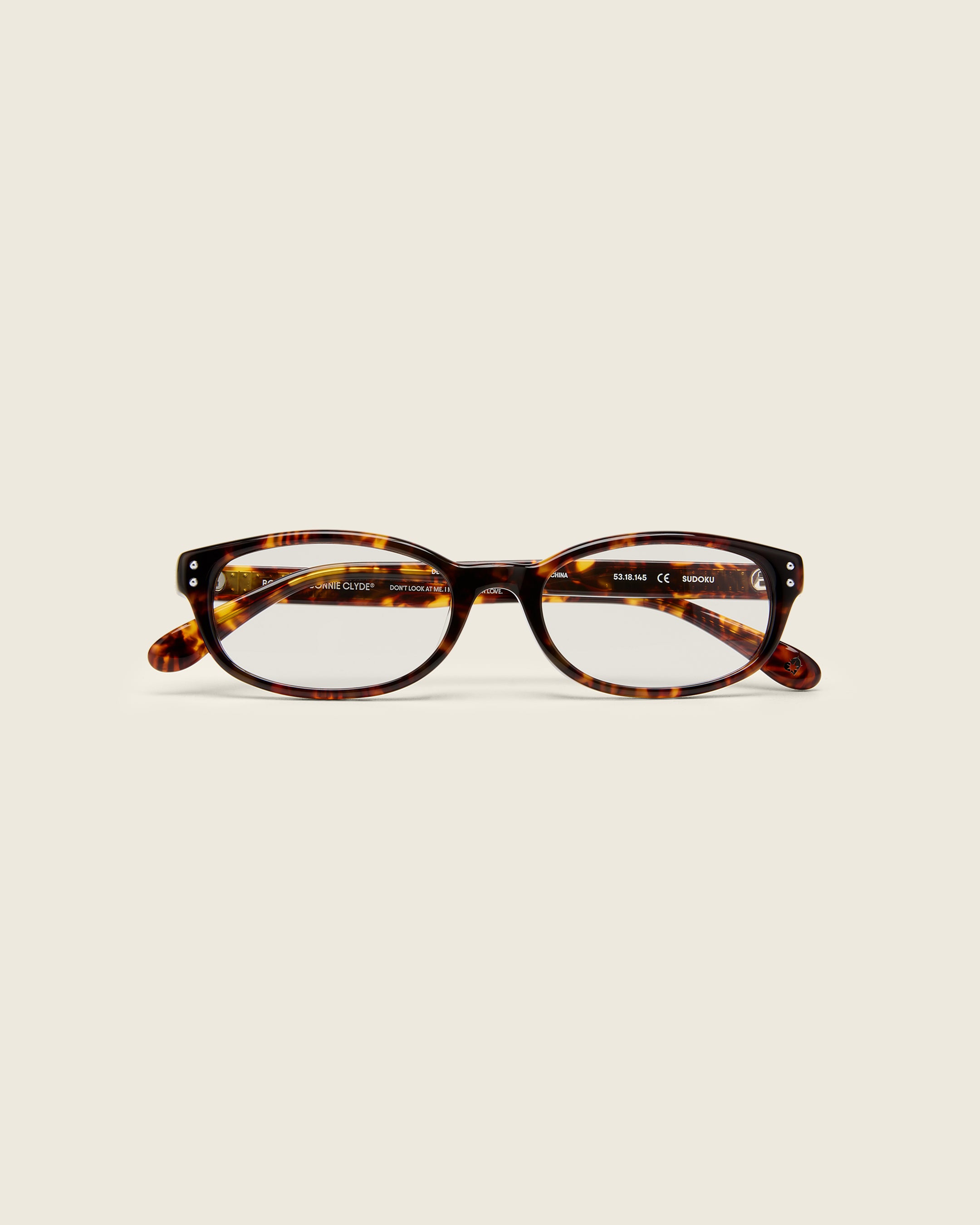 Tortoise acetate oval frames with a curved nosebridge and extended ear tips on a cream background. Face view. Double metal detailing on ear tips.
