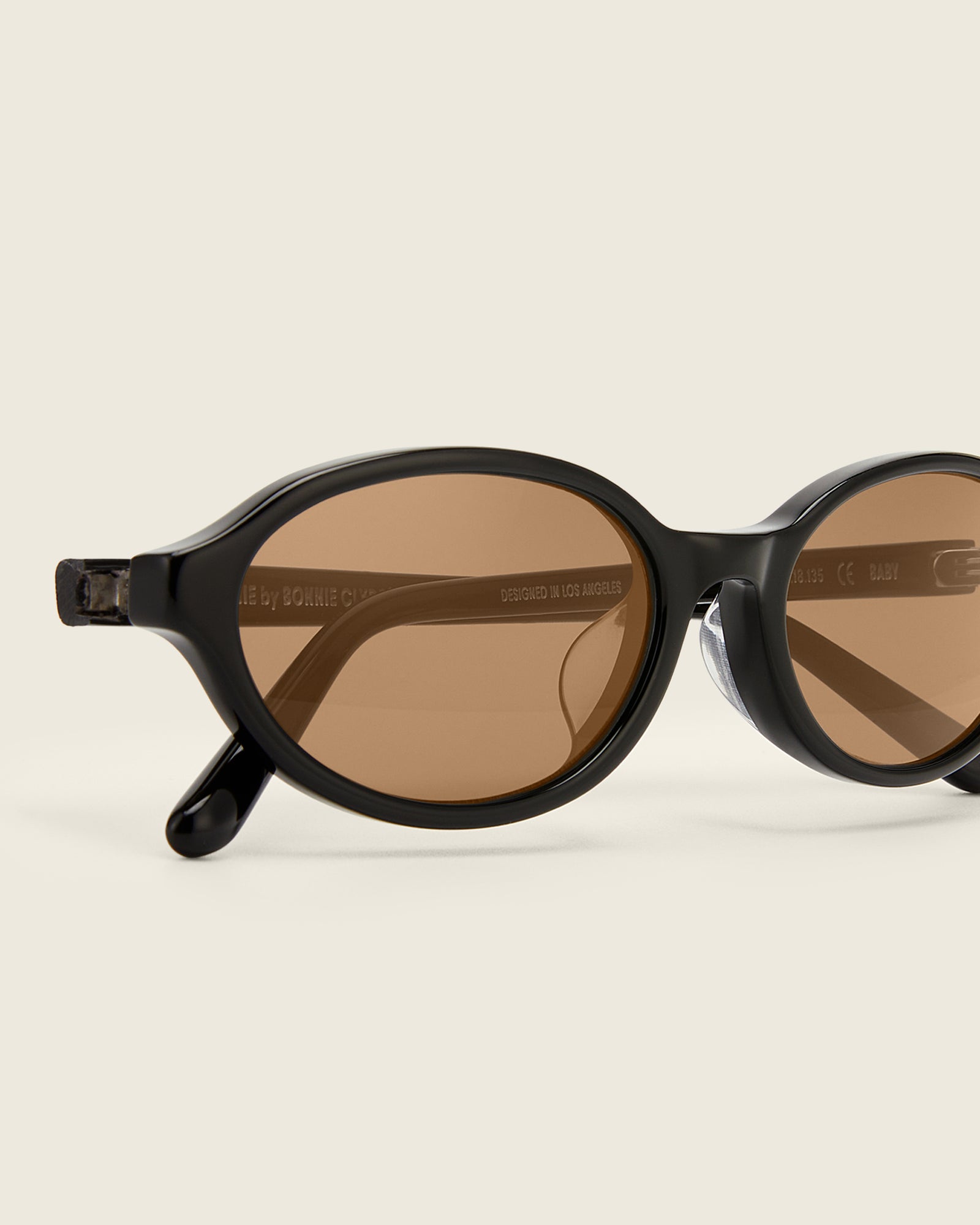 Bonnie Clyde Baby oval sunglasses in black acetate with brown lenses and double heart detailing on the arms, close-up view