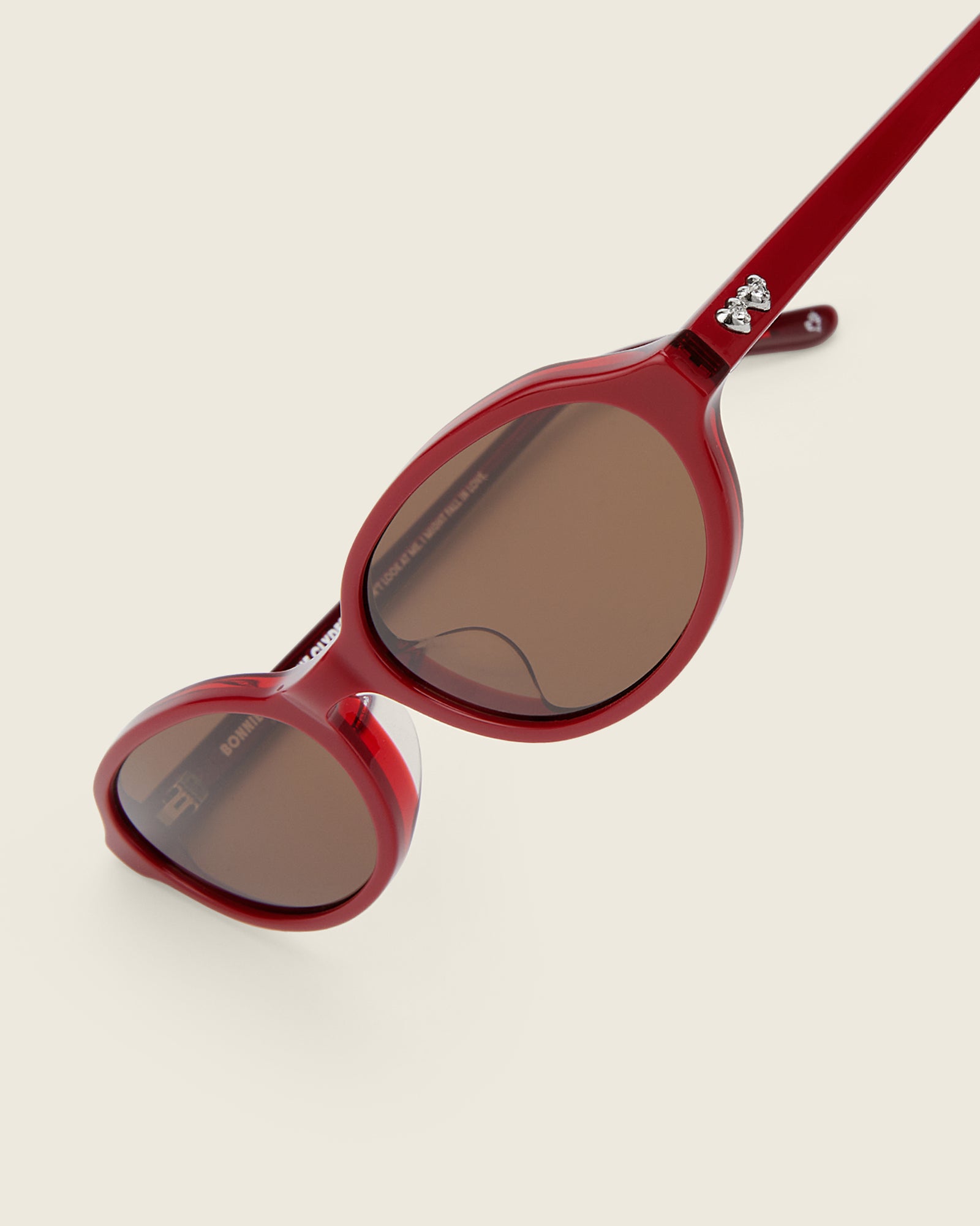 Bonnie Clyde red oval-shaped acetate sunglasses with brown lenses and double heart detailing on the arms, detail view