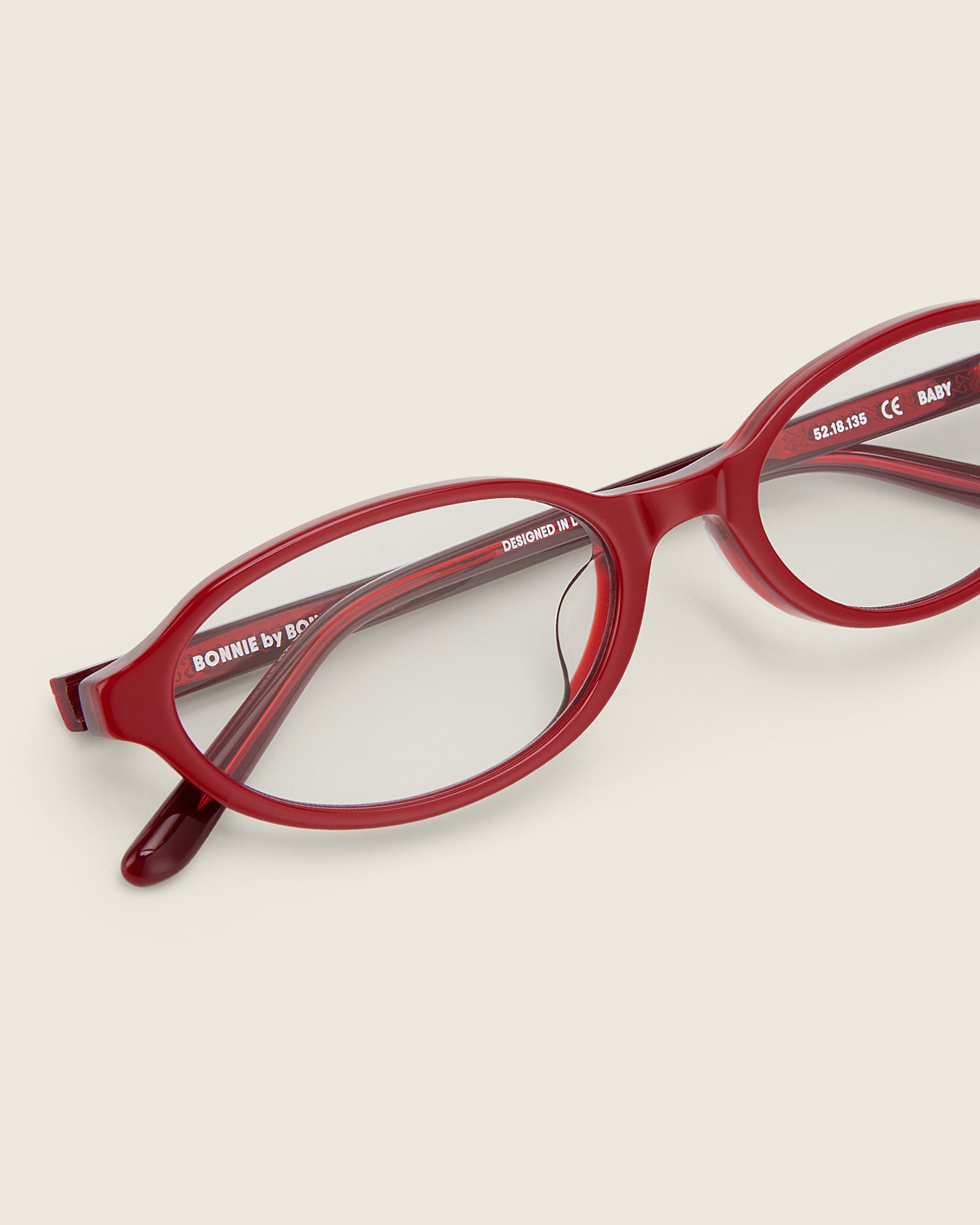 Bonnie Clyde close up of Red oval-shaped acetate glasses with clear lenses, featuring double heart detailing on the temples, close-up view