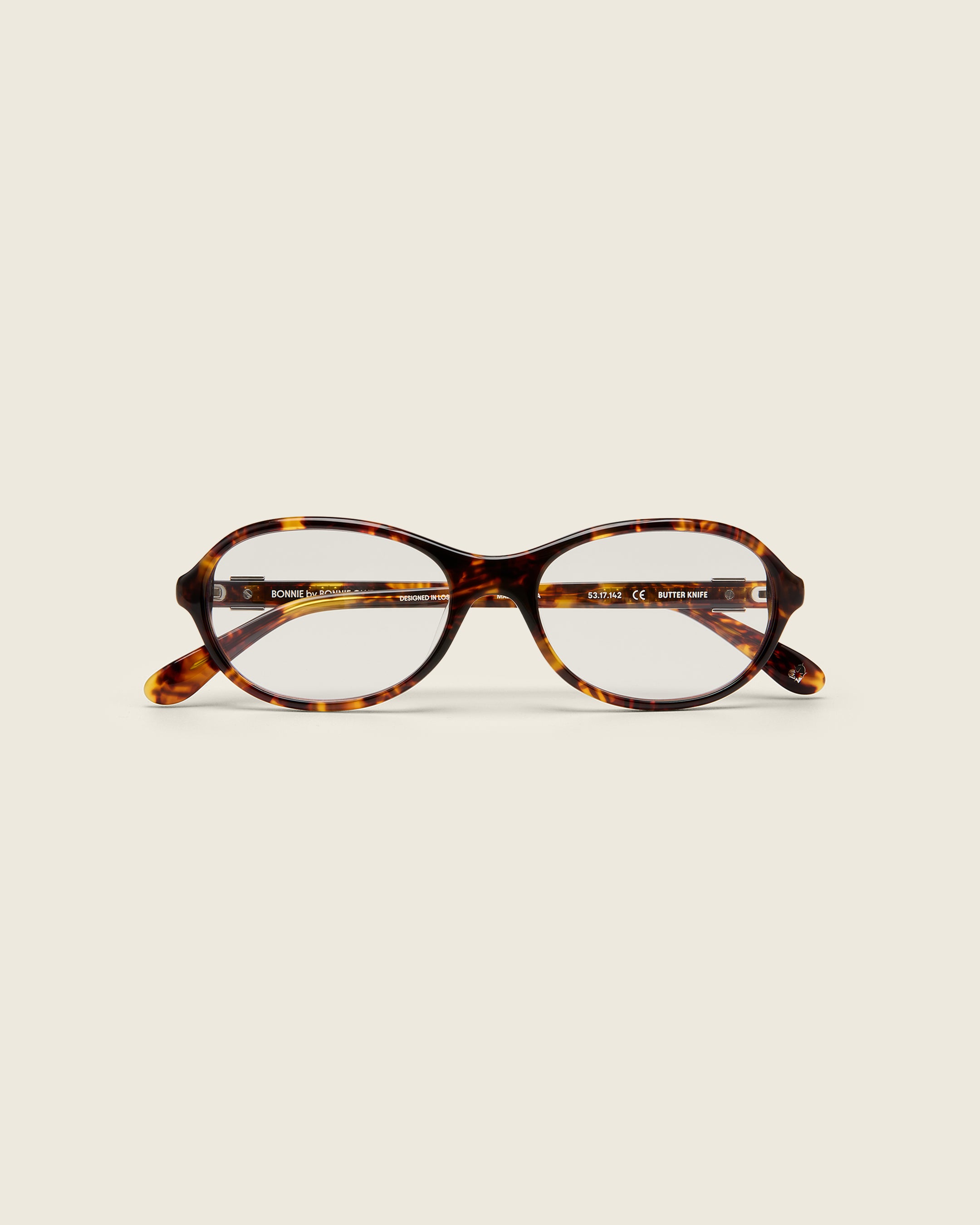 Rounded tortoise acetate frames. Features raised browline curvature on a beige background. Face view.