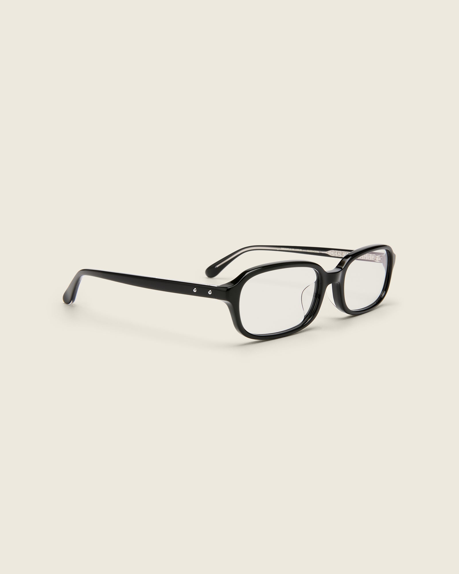 Rectangular black acetate frames with softened corners and a low-profile bridge on a beige background. Quarter view.