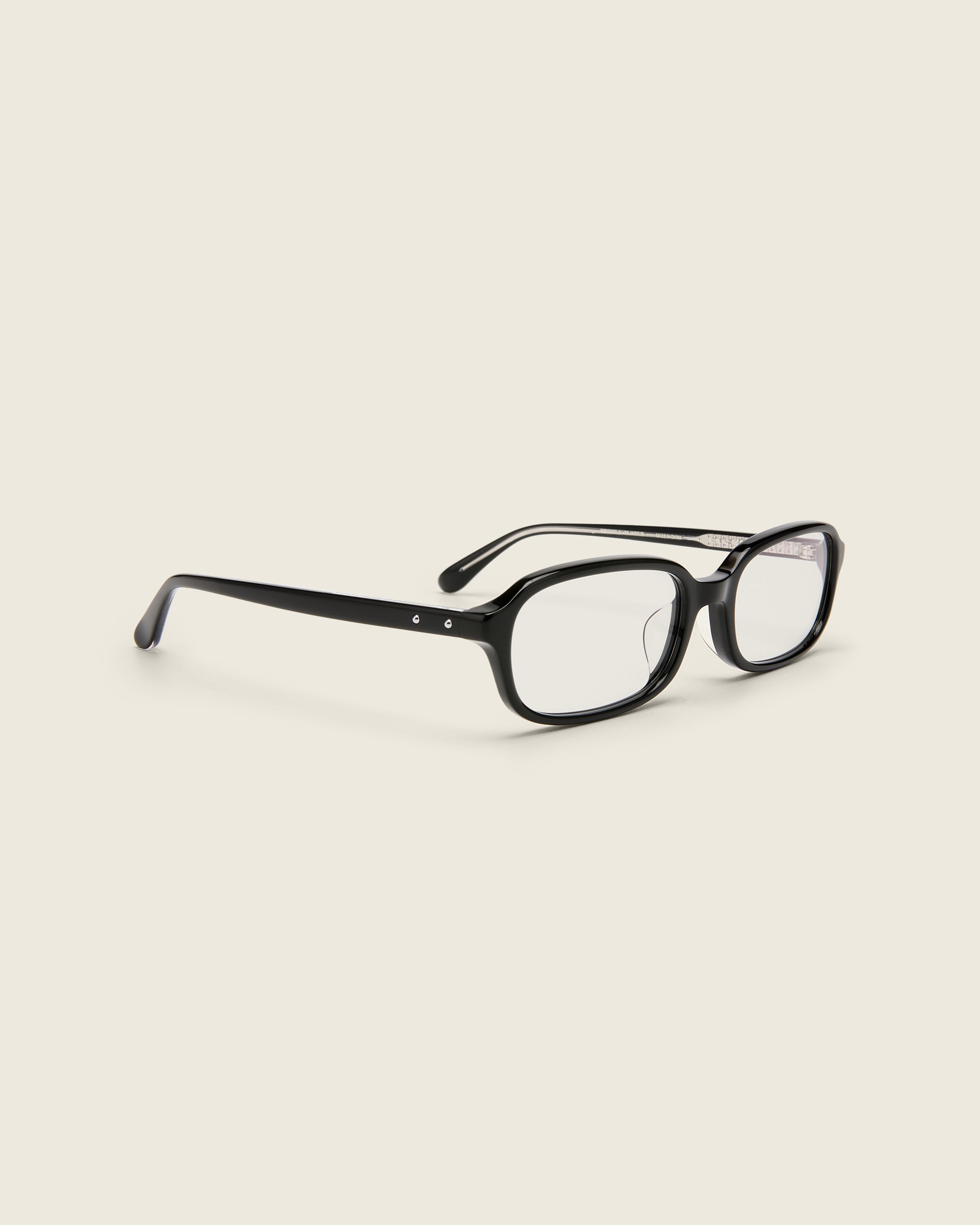 Rectangular black acetate frames with softened corners and a low-profile bridge on a beige background. Quarter view.