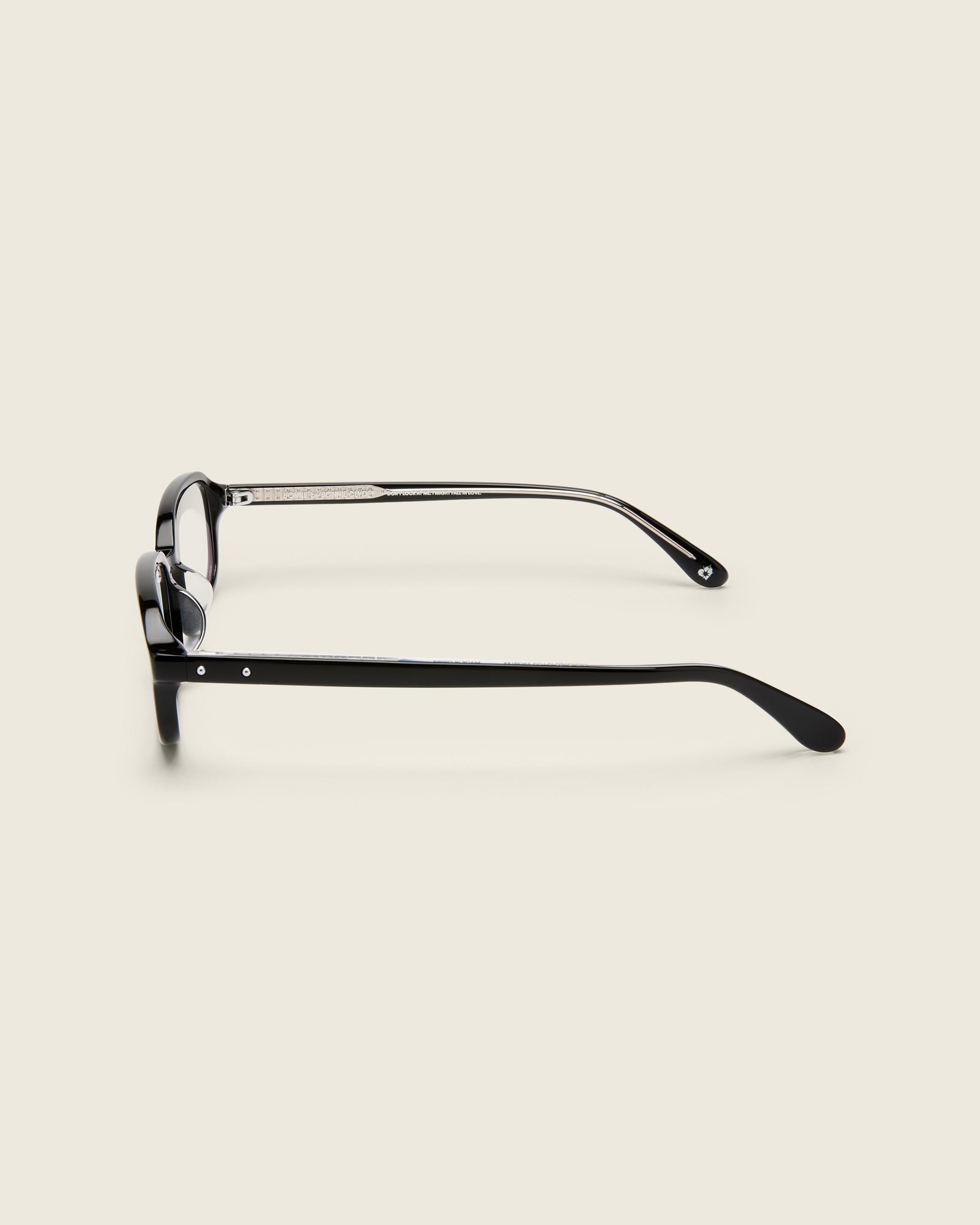 Rectangular black acetate frames with softened corners and a low-profile bridge on a beige background. Side view.