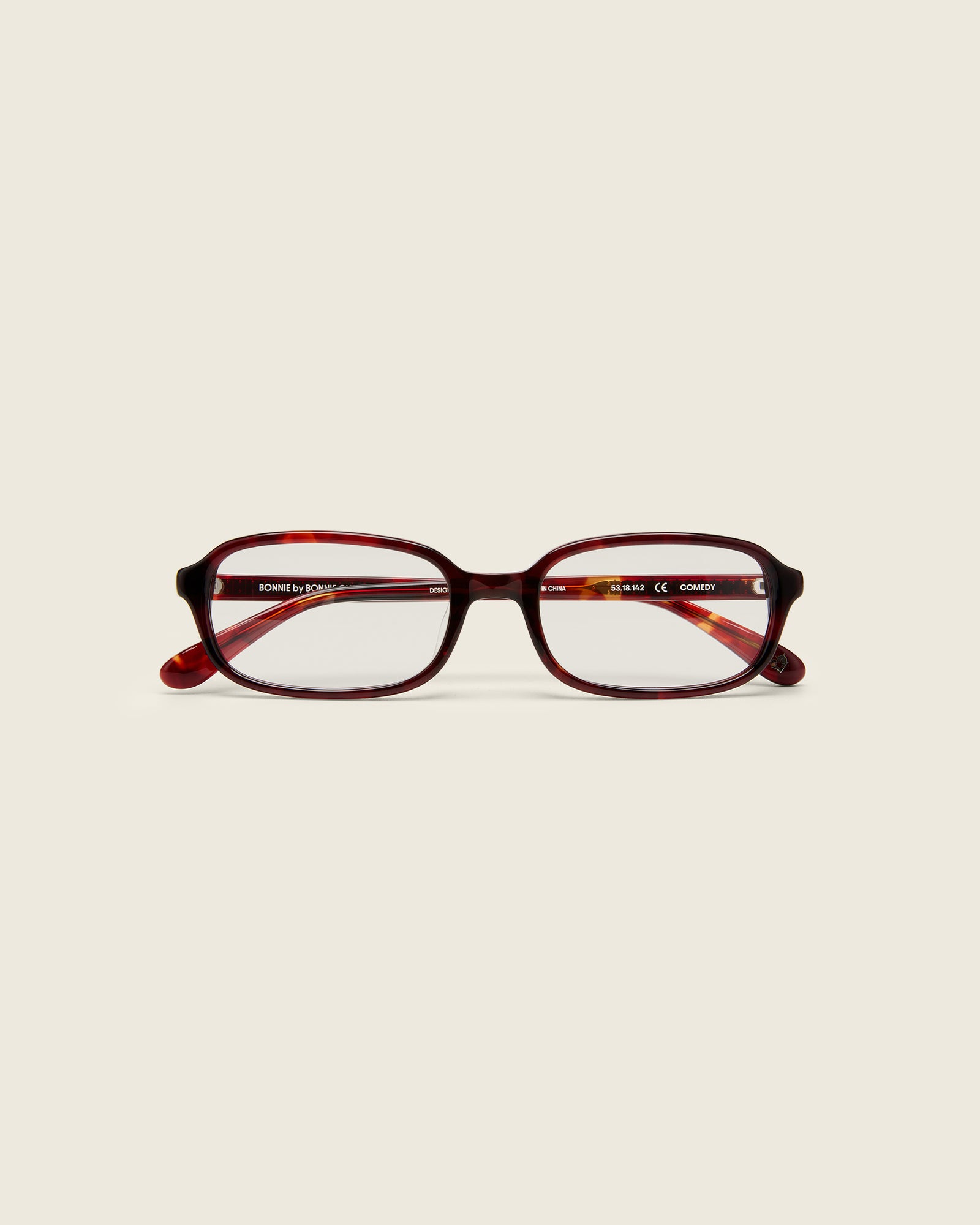 Rectangular red tortoise acetate frames with softened corners and a low-profile bridge on a beige background. Face view.