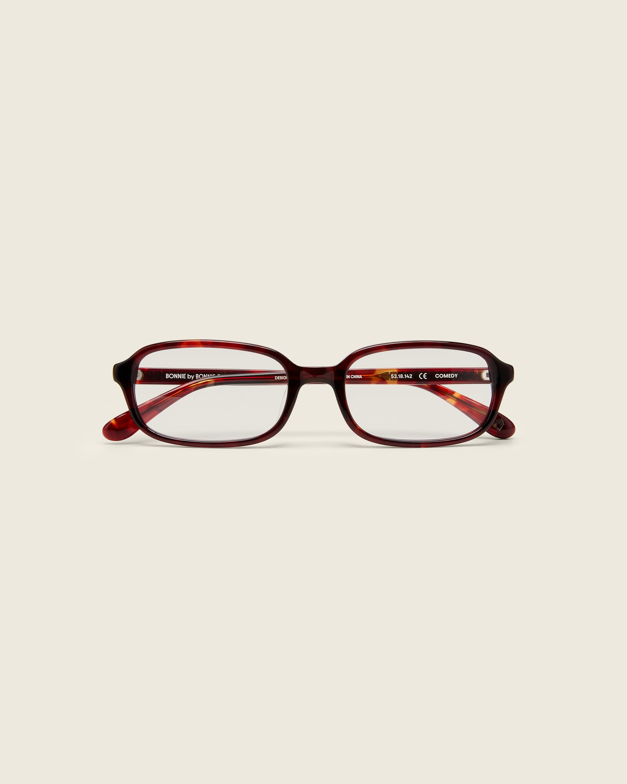 Rectangular red tortoise acetate frames with softened corners and a low-profile bridge on a beige background. Face view.