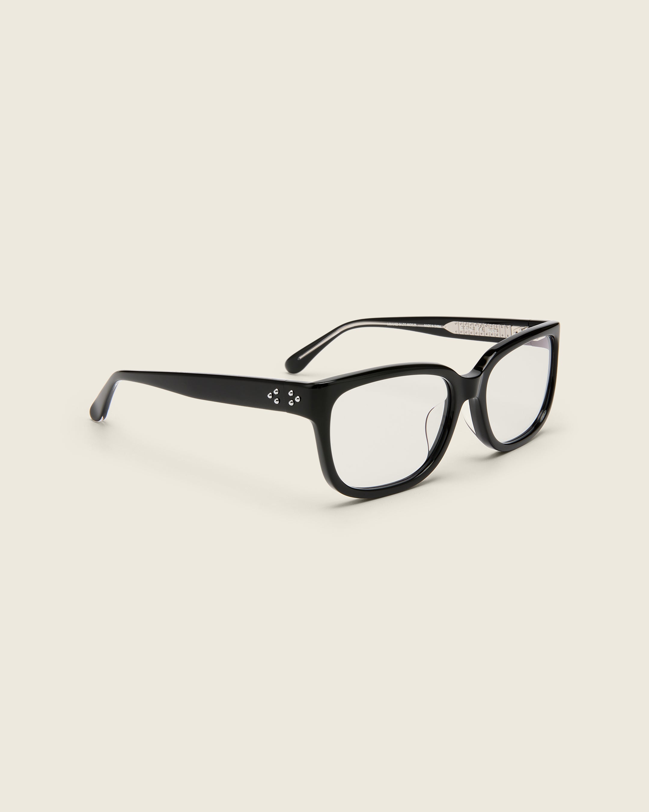 Bold, square-shaped black acetate frames on a beige background. Quarter view. Mirrored metal bead detail on arm temples.