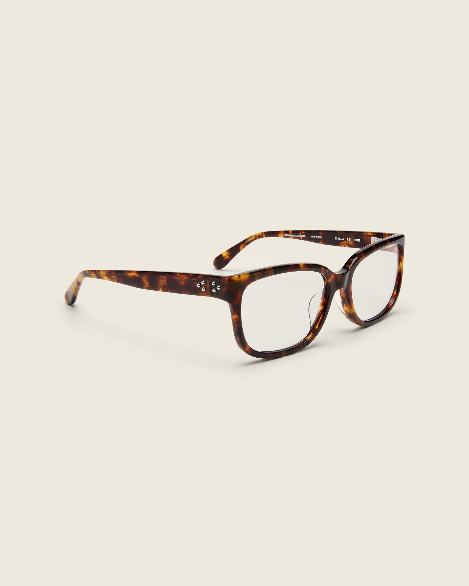 Bold, square-shaped tortoise acetate frames on a beige background. Quarter view. Mirrored metal bead detail on arm temples.