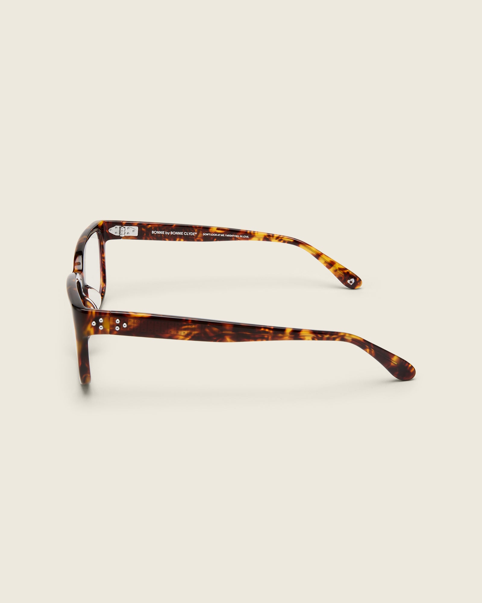 Bold, square-shaped tortoise acetate frames on a beige background. Side view. Mirrored metal bead detail on arm temples.