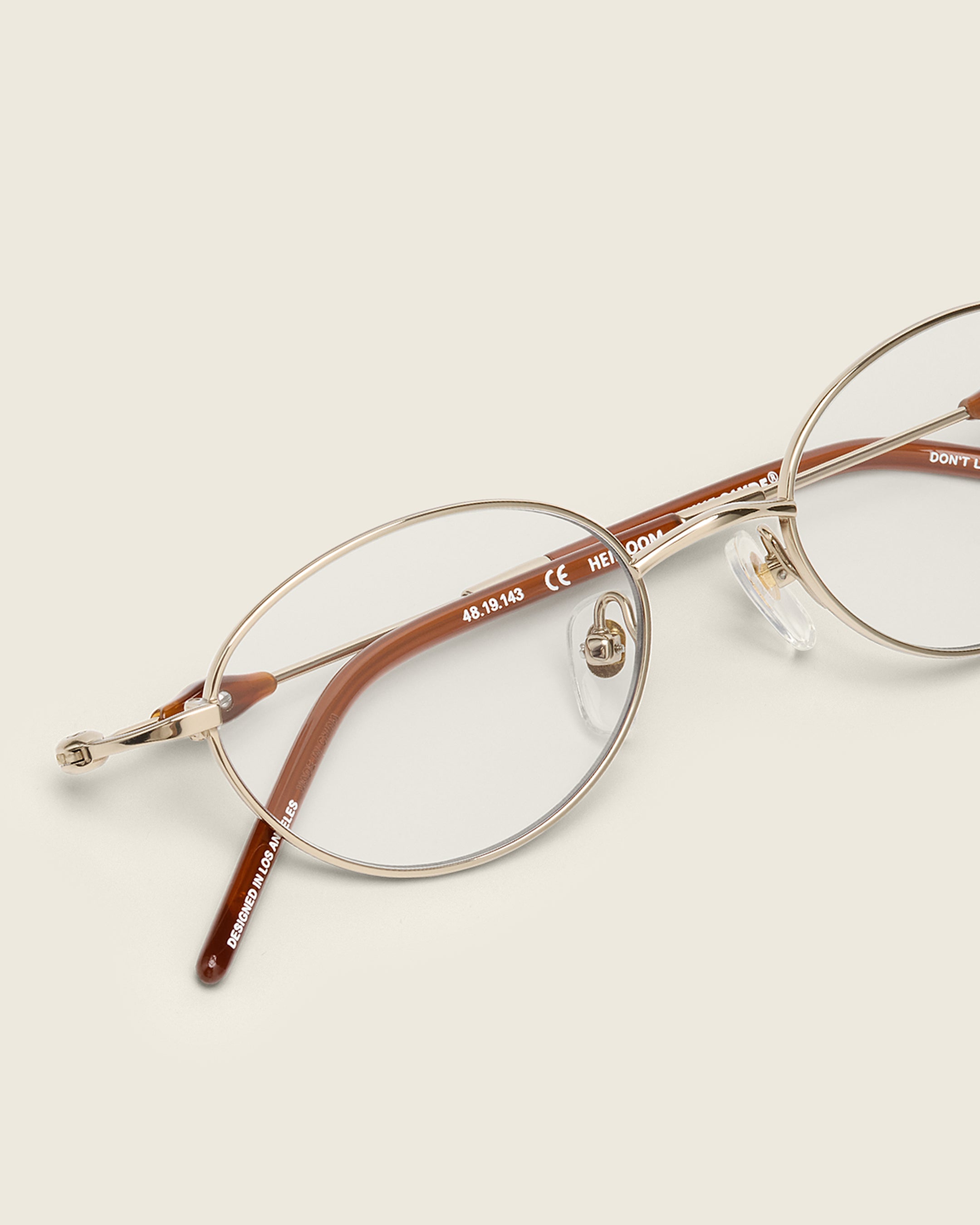 Slim, oval gold titanium frames with adjustable nose pads and lightweight acetate arm temple. Detail view.