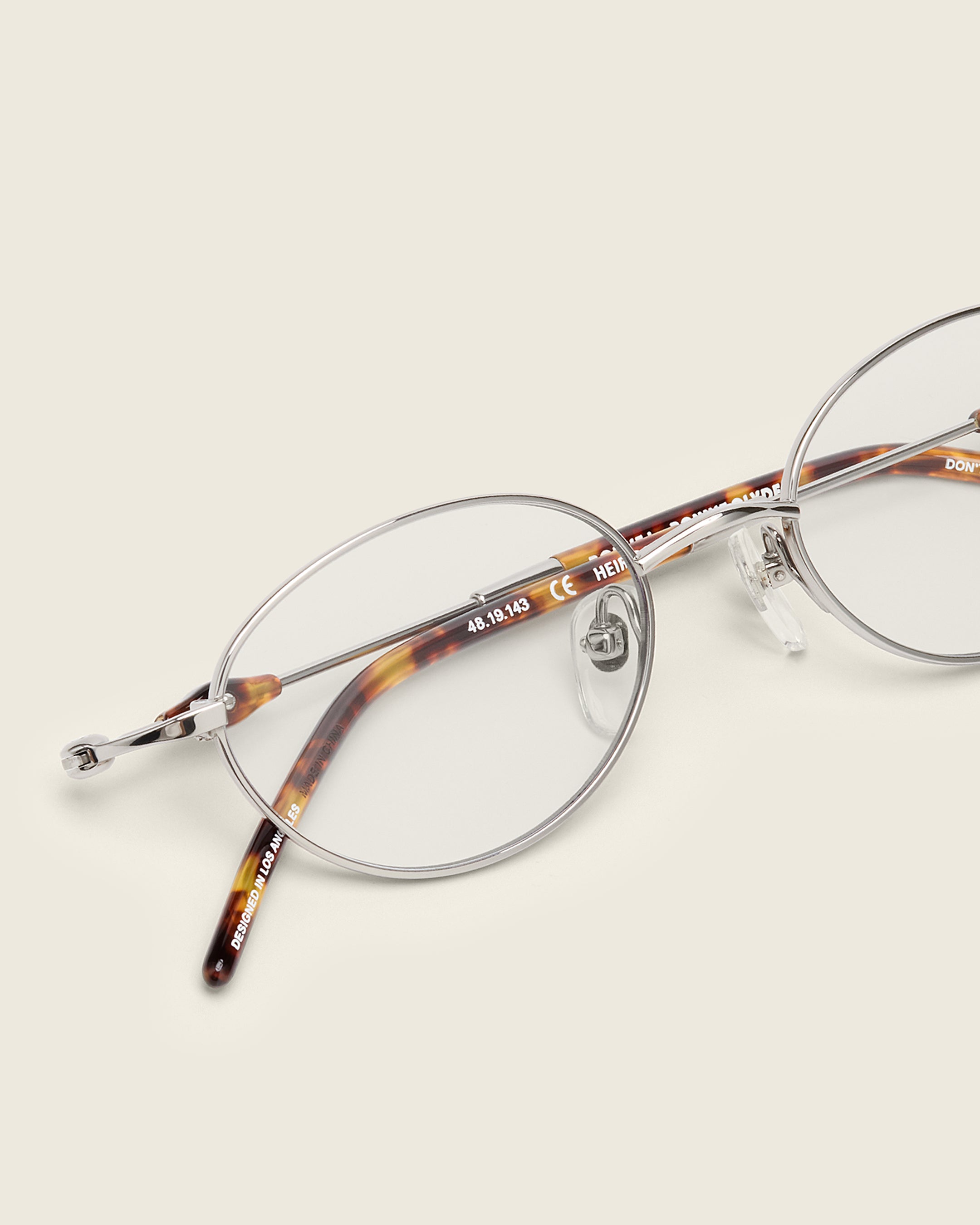 Slim, oval silver titanium frames with adjustable nose pads and lightweight acetate arm temple. Detail view.