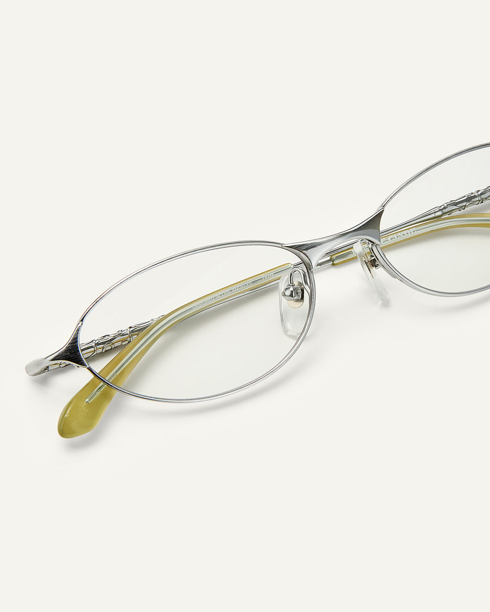 Close up shot of Bonnie Clyde Intro eyeglasses in silver titanium frames with green acetate details and clear lenses.