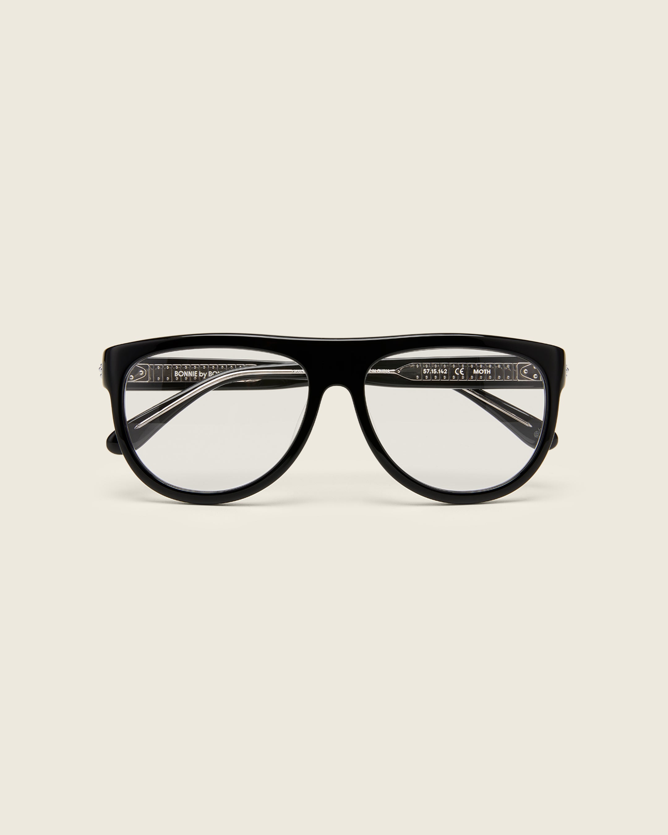 Oversized aviator-style black acetate frames with a bold browline and deep lenses on a cream background. Face view. 