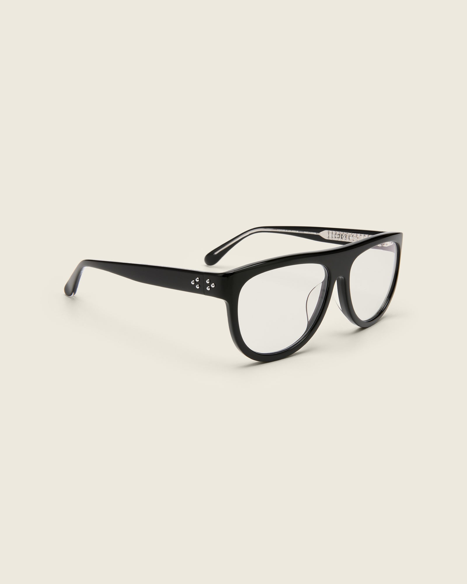 Oversized aviator-style black acetate frames with a bold browline and deep lenses on a cream background. Quarter view. Mirrored triple metal bead detailing on hinge and arm temple.