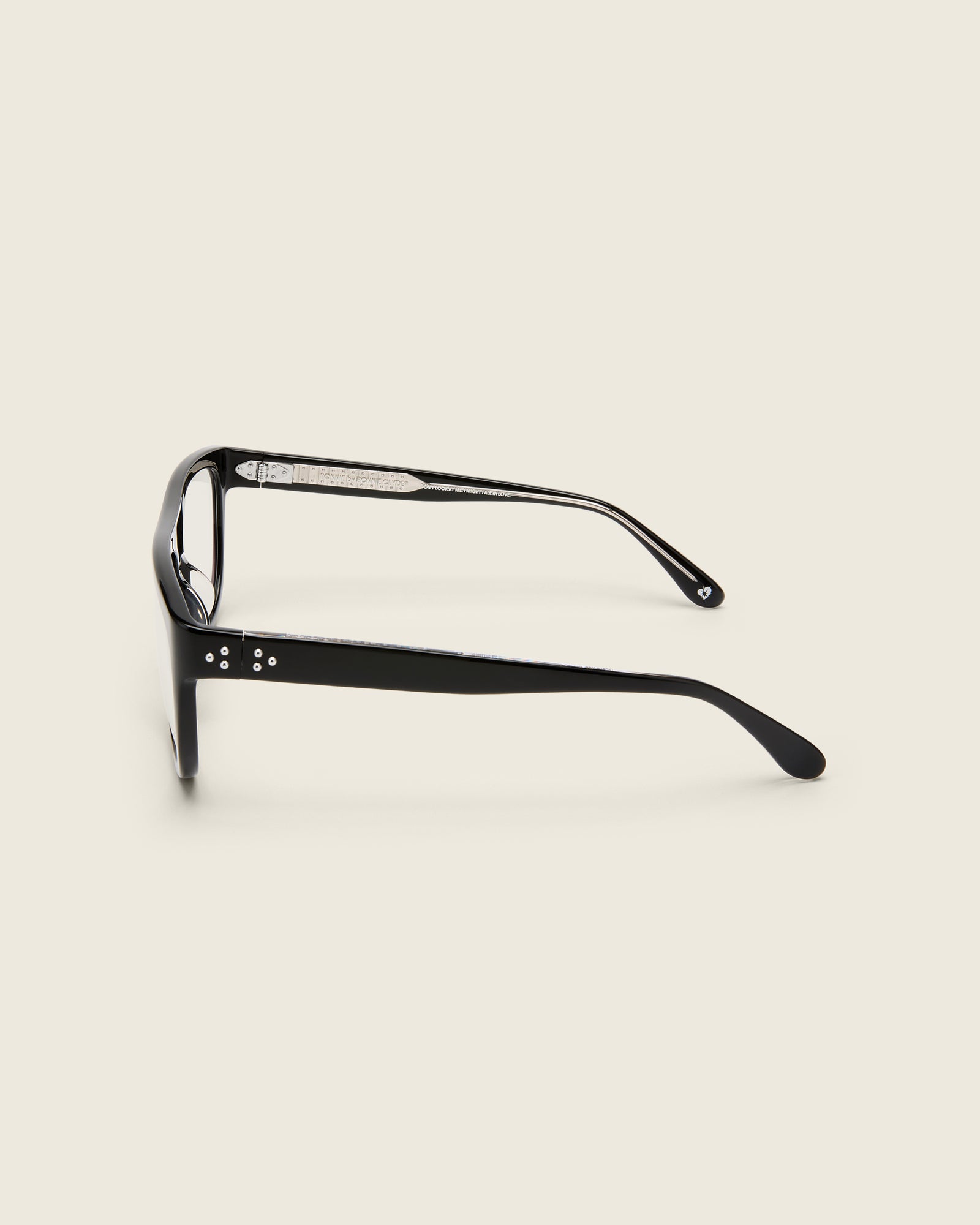Oversized aviator-style black acetate frames with a bold browline and deep lenses on a cream background. Side view. Mirrored triple metal bead detailing on hinge and arm temple.