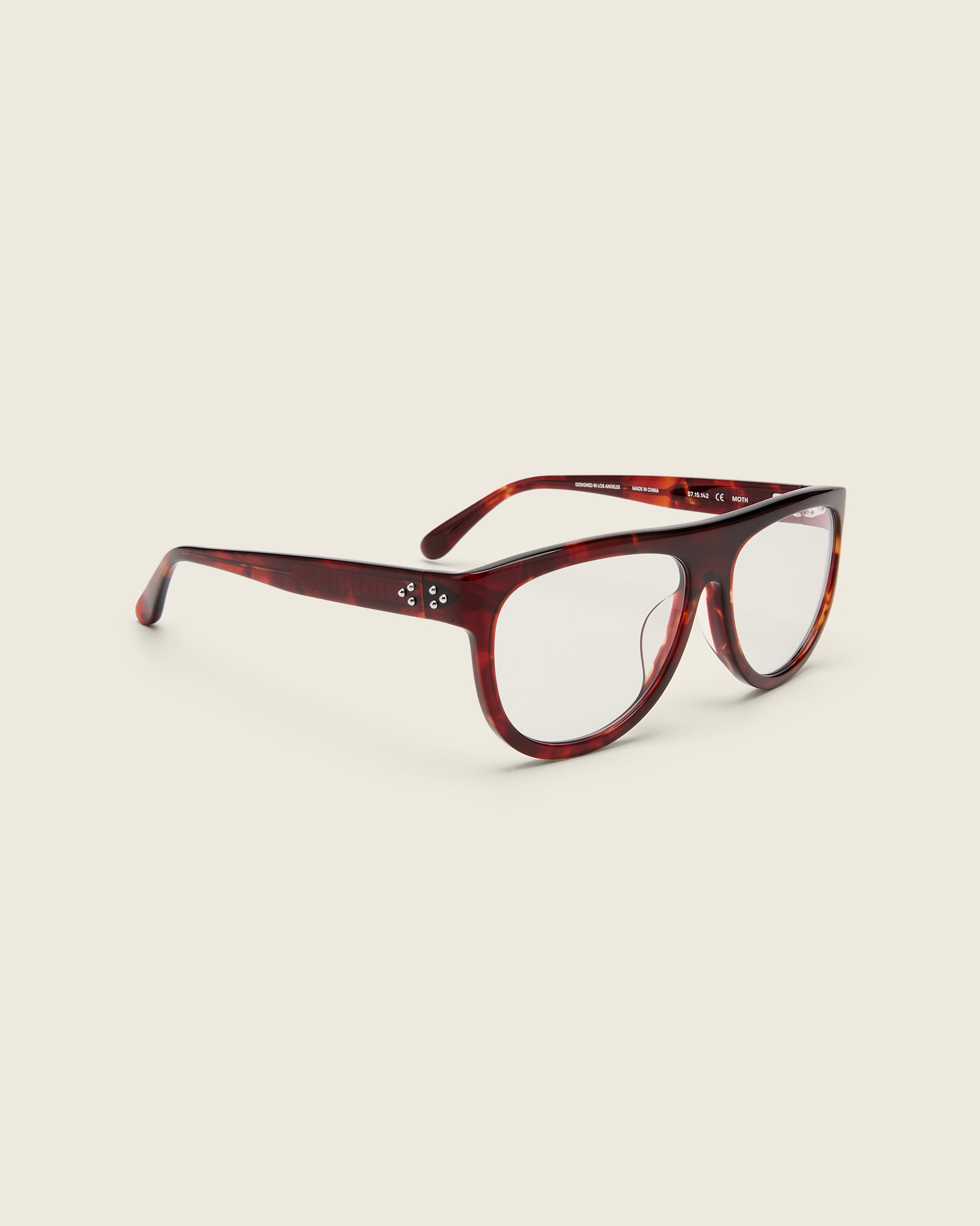 Oversized aviator-style red tortoise acetate frames with a bold browline and deep lenses on a cream background. Quarter view. Mirrored triple metal bead detailing on hinge and arm temple.