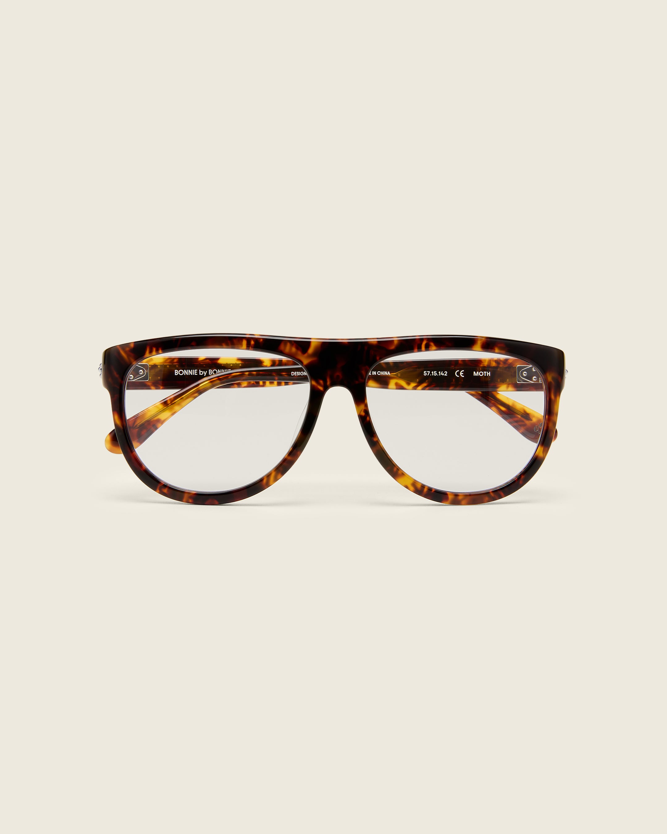 Oversized aviator-style tortoise acetate frames with a bold browline and deep lenses on a cream background. Face view. 