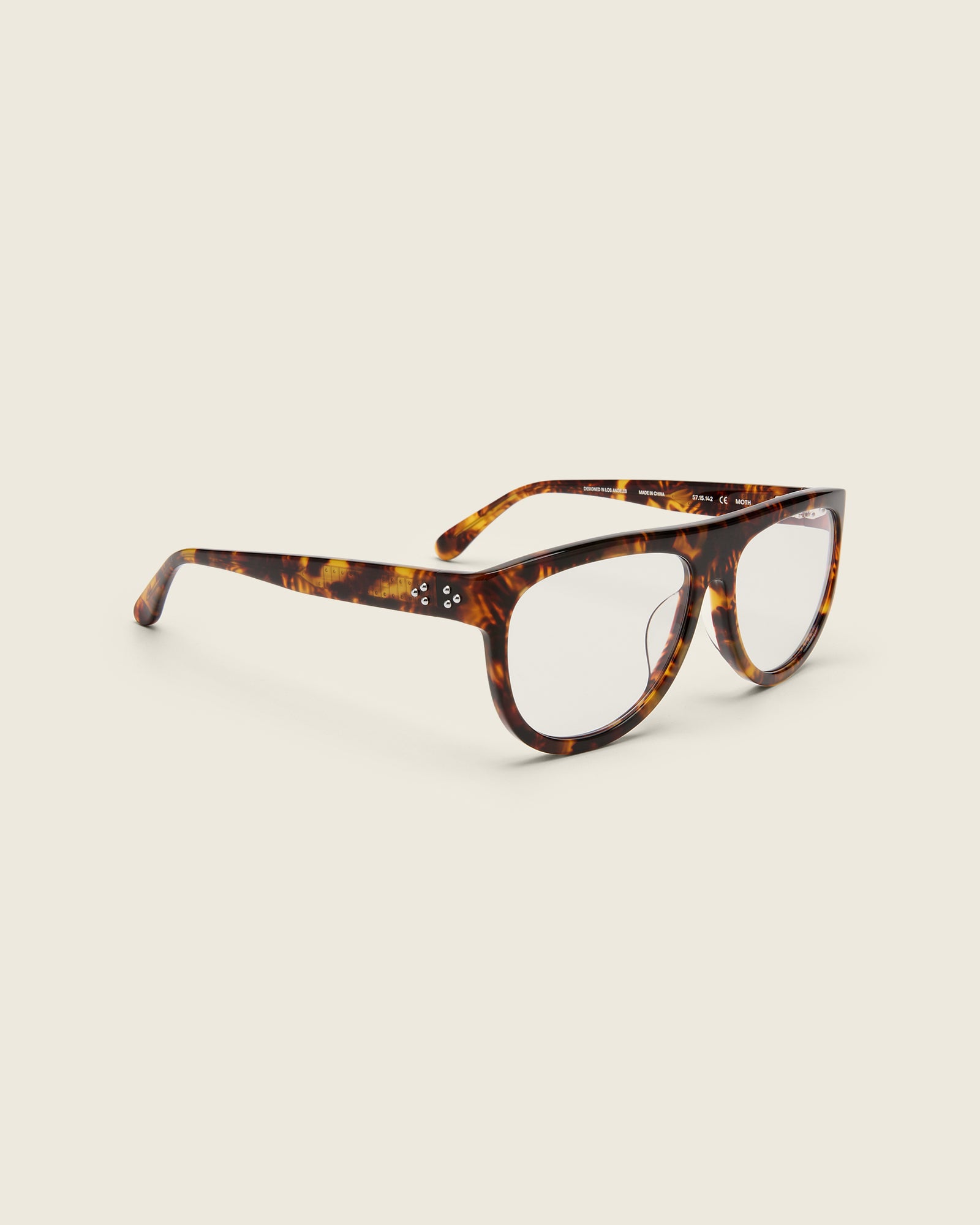 Oversized aviator-style tortoise acetate frames with a bold browline and deep lenses on a cream background. Quarter view. Mirrored triple metal bead detailing on hinge and arm temple.