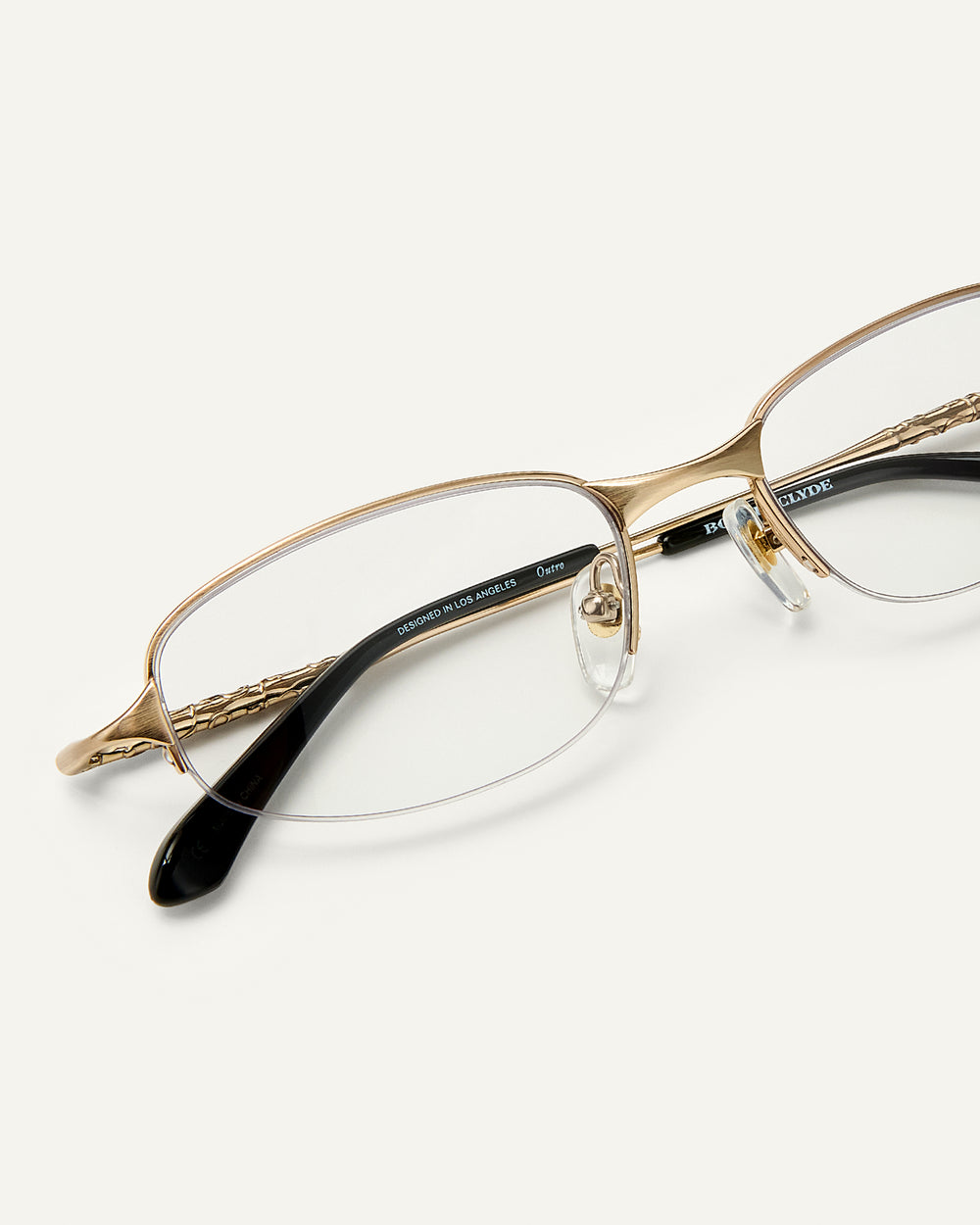 Close up shot of Bonnie Clyde Outro eyeglasses in gold titanium frames with black acetate details and clear lenses.