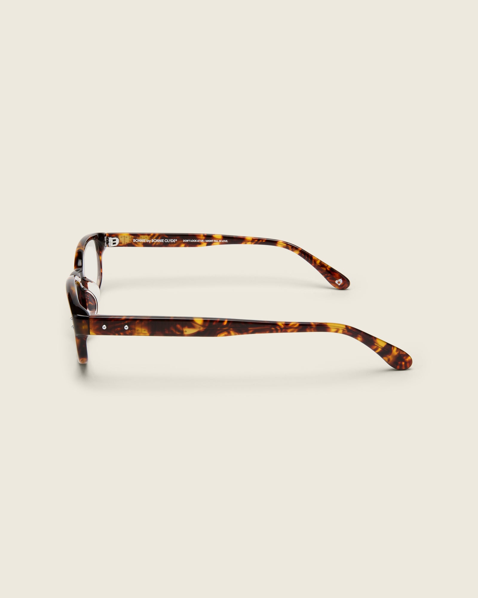Tortoise acetate oval frames with a curved nosebridge and extended ear tips on a cream background. Side view. Double metal detailing on arm temples.